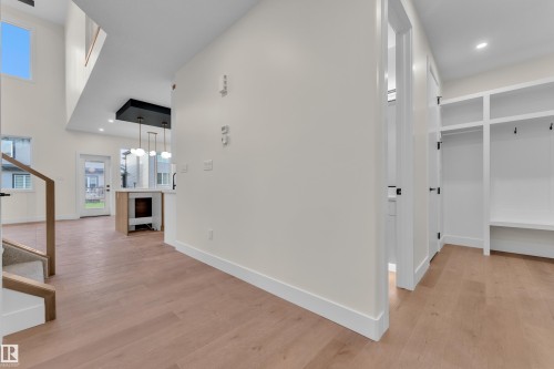 Open-concept interior featuring wood-finish flooring, a built-in mudroom bench with shelving, a two-story ceiling, a contemporary light fixture, and a built-in fireplace - 3602 44 Avenue, Beaumont, AB 