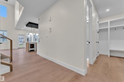 Open-concept interior featuring wood-finish flooring, a built-in mudroom bench with shelving, a two-story ceiling, a contemporary light fixture, and a built-in fireplace - 