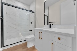 Bathroom featuring a walk-in shower with black-framed glass enclosure, white marble-look wall tiles, and black fixtures - 