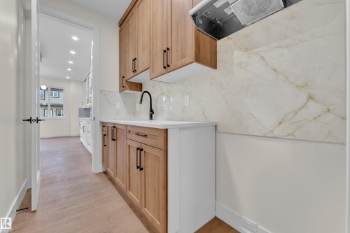 Kitchenette featuring light wood-finish cabinetry with matte black hardware, a pristine white countertop, and a contemporary matte black faucet - 3602 44 Avenue, Beaumont, AB 