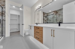 Dual vanity featuring white shaker cabinetry with gold-tone hardware, a central wood-finish drawer stack, and solid surface countertops - 