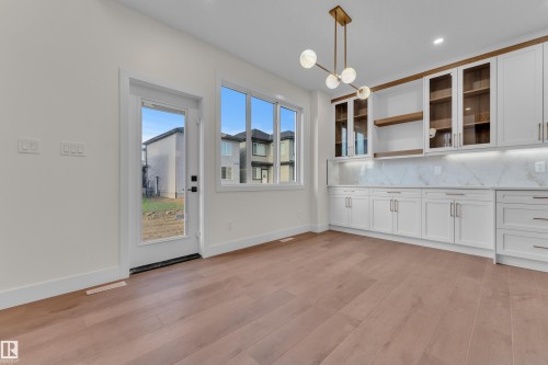 Open concept room featuring wood-finish flooring, white cabinetry with gold-tone hardware, and a contemporary chandelier - 3602 44 Avenue, Beaumont, AB 