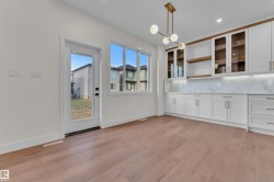 Open concept room featuring wood-finish flooring, white cabinetry with gold-tone hardware, and a contemporary chandelier - 