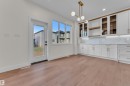 Open concept room featuring wood-finish flooring, white cabinetry with gold-tone hardware, and a contemporary chandelier - 3602 44 Avenue, Beaumont, AB 