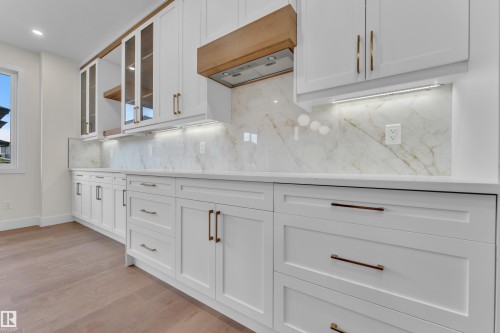 White shaker cabinetry featuring gold-finish hardware, a natural wood range hood, and integrated under-cabinet lighting - 3602 44 Avenue, Beaumont, AB 
