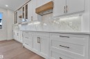 White shaker cabinetry featuring gold-finish hardware, a natural wood range hood, and integrated under-cabinet lighting - 3602 44 Avenue, Beaumont, AB 