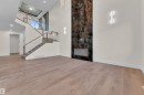 Two-story living area featuring a prominent dark marble-look fireplace with an integrated hearth, light wood-finish flooring, and a contemporary open-riser staircase with glass railings and wood handrails - 3602 44 Avenue, Beaumont, AB 