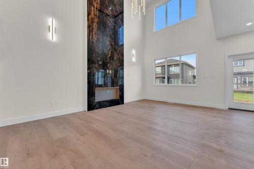 Two-story living area featuring a full-height black and gold marbled accent wall with an integrated linear fireplace, light wood-finish flooring, and multiple windows providing ample natural light - 3602 44 Avenue, Beaumont, AB 