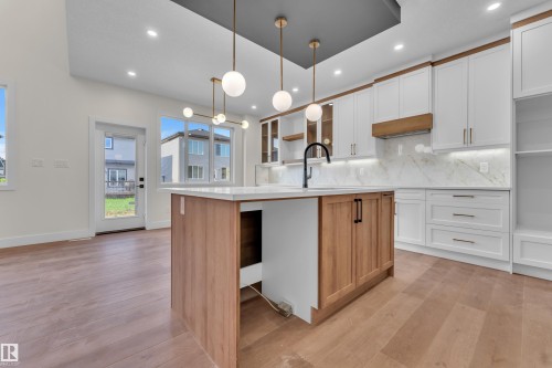 Bright kitchen featuring a central island with wood-finish paneling, white countertops, and a black gooseneck faucet - 3602 44 Avenue, Beaumont, AB 