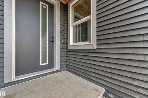 Entryway featuring a dark gray door with a vertical glass insert, white trim, horizontal siding, and a concrete landing - 3602 44 Avenue, Beaumont, AB 