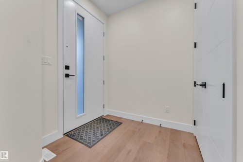 Entryway featuring light wood-finish flooring, a contemporary white door with a frosted vertical glass panel, and matte black hardware - 3602 44 Avenue, Beaumont, AB 