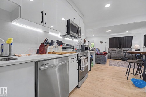 Modern kitchen featuring white cabinetry, light countertops, stainless steel appliances, and integrated under-cabinet lighting - 11914 124 Street, Edmonton, AB 