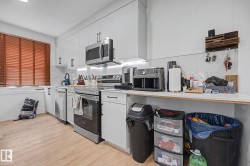 Modern kitchen featuring white cabinetry, stainless steel appliances, light wood-finish flooring, and white countertops - 