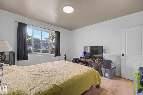 Spacious room featuring a large window, a modern ceiling light fixture, wood-finish flooring, and a paneled interior door with black hardware - 11914 124 Street, Edmonton, AB 