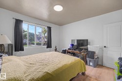 Spacious room featuring a large window, a modern ceiling light fixture, wood-finish flooring, and a paneled interior door with black hardware - 