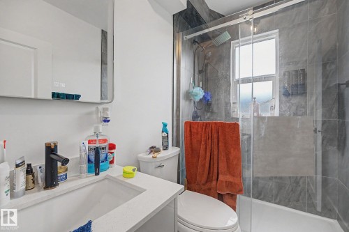 Bathroom featuring a glass-enclosed shower with gray tiled walls, a white vanity with an integrated sink and white countertop, a black faucet, and a wall-mounted mirrored cabinet - 11914 124 Street, Edmonton, AB 