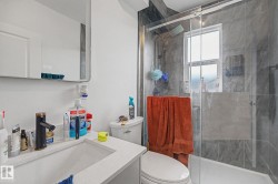 Bathroom featuring a glass-enclosed shower with gray tiled walls, a white vanity with an integrated sink and white countertop, a black faucet, and a wall-mounted mirrored cabinet - 