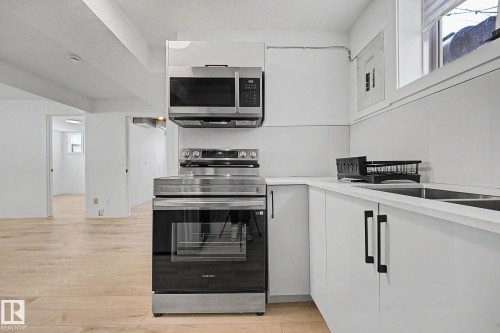 Contemporary kitchen featuring white cabinetry, a stainless steel electric range, an over-range microwave, and a double basin sink - 11914 124 Street, Edmonton, AB 