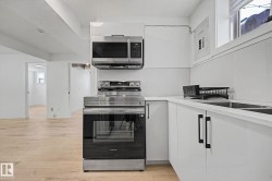 Contemporary kitchen featuring white cabinetry, a stainless steel electric range, an over-range microwave, and a double basin sink - 