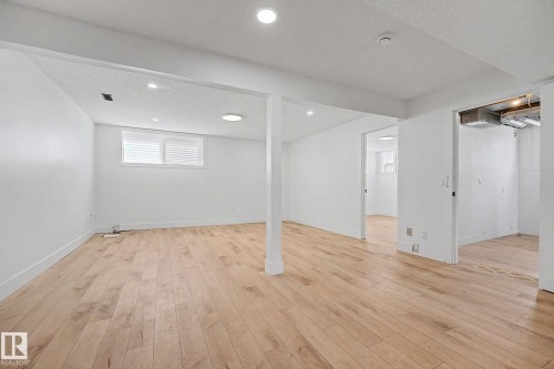Spacious room featuring wood-finish flooring, white walls, and recessed lighting - 11914 124 Street, Edmonton, AB 