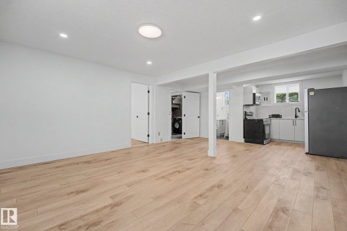 Open-concept living area featuring light wood-finish flooring, recessed lighting, and a modern kitchen with white cabinetry - 11914 124 Street, Edmonton, AB 