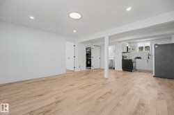 Open-concept living area featuring light wood-finish flooring, recessed lighting, and a modern kitchen with white cabinetry - 