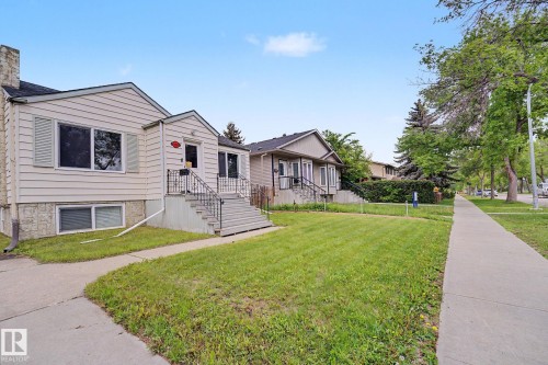 Exterior featuring light-colored siding, a prominent front entrance with stairs and railings, and a concrete sidewalk - 11914 124 Street, Edmonton, AB 