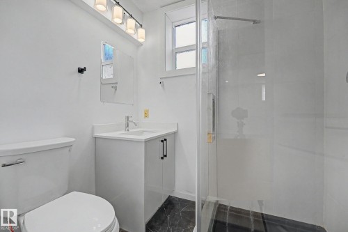 Bathroom featuring a glass-enclosed shower, a white vanity with a single sink, and a modern light fixture - 11914 124 Street, Edmonton, AB 