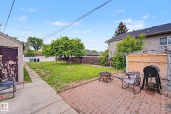 Expansive backyard featuring a mature tree, a paved brick patio, and a grass lawn - 