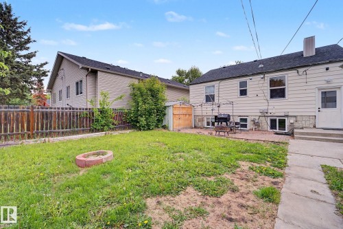 Expansive backyard featuring a lush lawn, a brick-lined fire pit, a paved patio area, and a wood-panel storage shed - 11914 124 Street, Edmonton, AB 