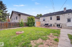 Expansive backyard featuring a lush lawn, a brick-lined fire pit, a paved patio area, and a wood-panel storage shed - 