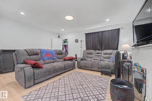 Light wood-finish flooring provides a neutral base for this living area, featuring recessed ceiling lighting and a central flush-mount fixture - 11914 124 Street, Edmonton, AB 