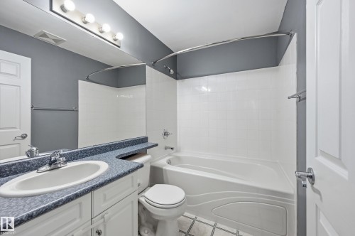 Bathroom featuring a white vanity with cabinet storage, a speckled blue countertop, an undermount sink, and a chrome faucet - 203 11103 84 Avenue, Edmonton, AB 