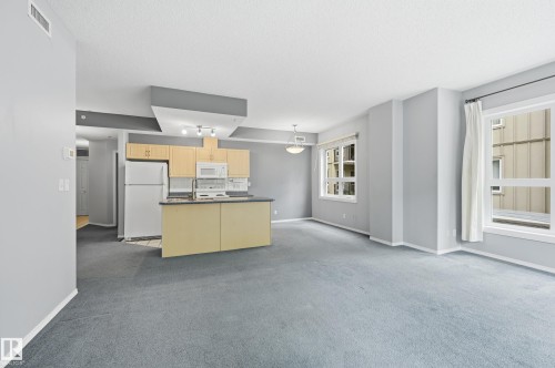 Open-concept living space featuring a kitchen with light wood-finish cabinetry, a white appliance package, and a breakfast bar - 203 11103 84 Avenue, Edmonton, AB 