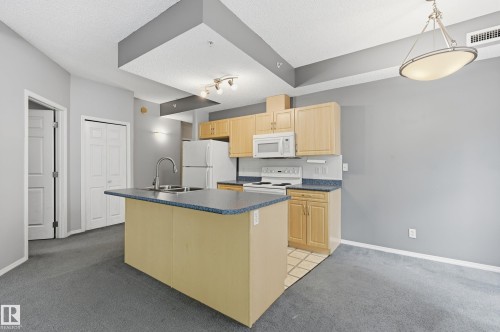Kitchen featuring light wood-finish cabinetry, white appliances, and a central island with a double basin sink - 203 11103 84 Avenue, Edmonton, AB 