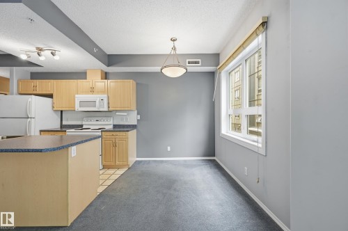 Open concept living space featuring a kitchen island with a dark countertop, light wood-finish cabinetry, and white appliances - 203 11103 84 Avenue, Edmonton, AB 