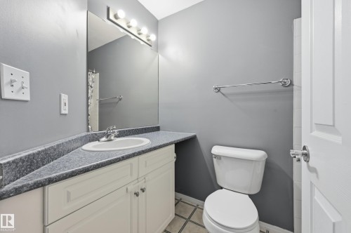 Bathroom featuring a vanity with an integrated sink, a speckled countertop, and white cabinetry with chrome hardware - 203 11103 84 Avenue, Edmonton, AB 