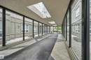 Enclosed walkway featuring a patterned tile floor with a carpet runner, multiple skylights, and full-height windows on both sides - 203 11103 84 Avenue, Edmonton, AB 