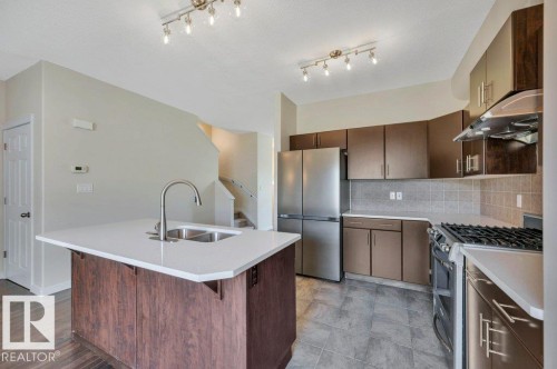 Kitchen featuring a central island with an undermount double sink, a gooseneck faucet, and a light-toned countertop - 14 4367 Veterans Way, Edmonton, AB 