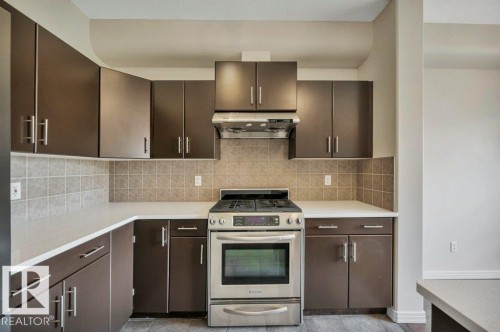 Contemporary kitchen featuring dark wood-finish cabinetry with brushed nickel hardware, light-toned countertops, and a full tile backsplash - 14 4367 Veterans Way, Edmonton, AB 