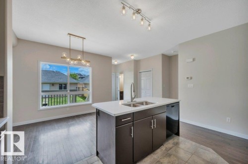 Kitchen island featuring a double-basin sink with a gooseneck faucet, dark cabinetry, and a light-toned countertop - 14 4367 Veterans Way, Edmonton, AB 