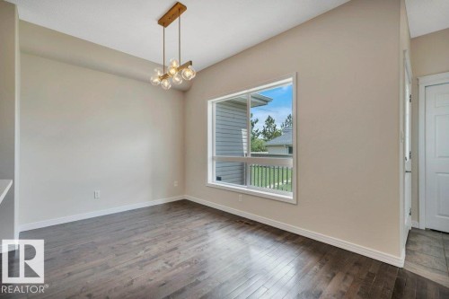 Spacious room featuring wood-finish flooring, a large window, and a contemporary ceiling light fixture - 14 4367 Veterans Way, Edmonton, AB 