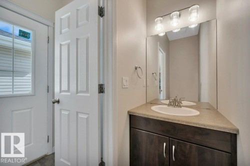 Vanity featuring a built-in sink, brushed nickel faucet, and a large mirror with a three-light fixture - 14 4367 Veterans Way, Edmonton, AB 
