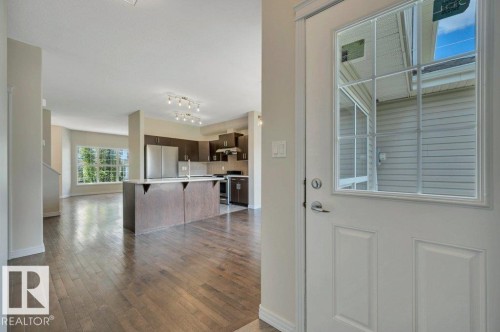Entryway featuring a white paneled door with an upper window insert, opening to an expansive interior with wood-finish flooring - 14 4367 Veterans Way, Edmonton, AB 