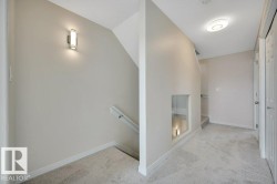 Carpeted hallway featuring a built-in wall niche with glass paneling, overhead flush mount lighting, and contrasting baseboards - 