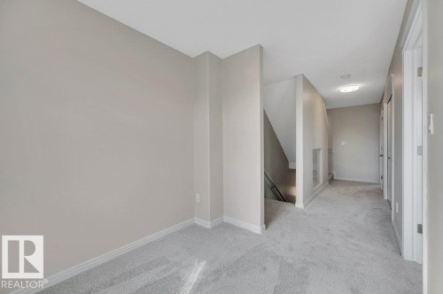 Open common area featuring light gray wall paint, white trim, light gray carpeting, and a flush-mount ceiling light - 14 4367 Veterans Way, Edmonton, AB 