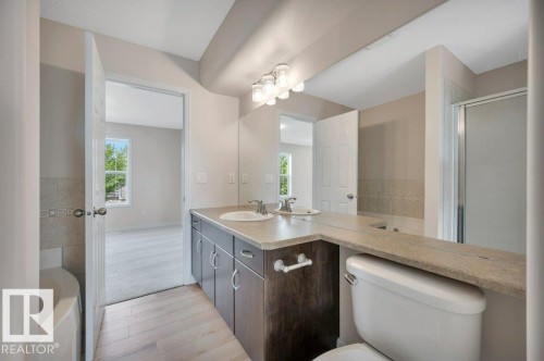 Bathroom featuring a dual vanity with undermount sinks, light-toned countertop, and wood-finish cabinetry - 14 4367 Veterans Way, Edmonton, AB 