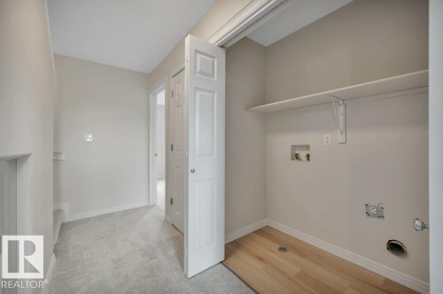 Utility closet featuring wood-finish flooring, a built-in shelf, and appliance hookups - 14 4367 Veterans Way, Edmonton, AB 