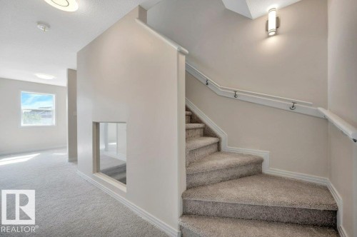 Carpeted staircase with white handrail and wall-mounted lighting - 14 4367 Veterans Way, Edmonton, AB 