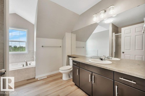 Bathroom featuring a dual vanity with dark wood-finish cabinetry, a large mirror, a separate shower enclosure, a bathtub with tiled surround, and wood-finish flooring - 14 4367 Veterans Way, Edmonton, AB 